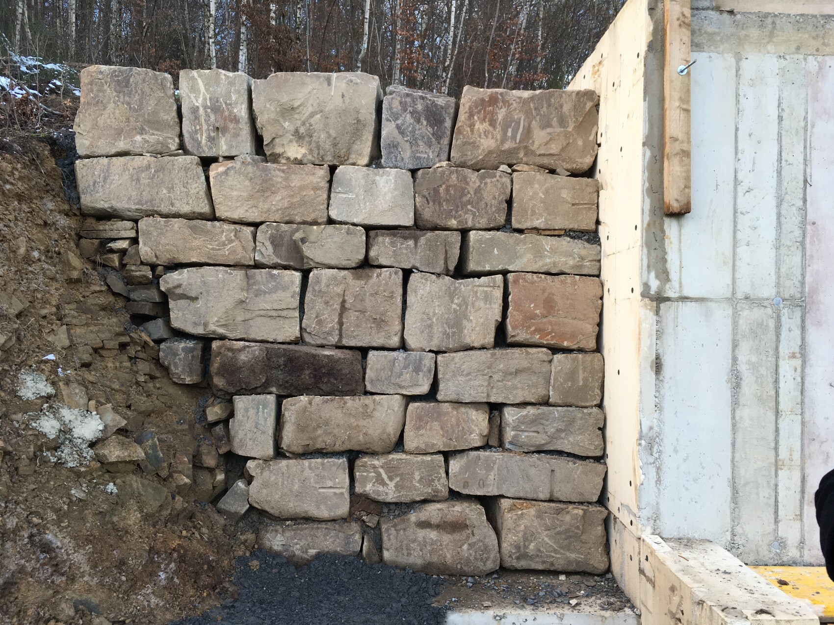 Retaining wall made of rough natural stone blocks, built next to a building structure.