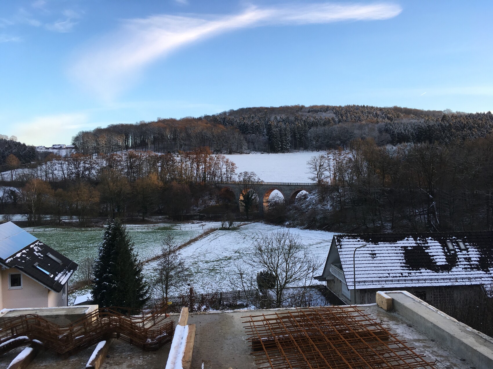 Winter landscape with snow-covered valley and viaduct, forest, houses, and reinforcement steel in the foreground