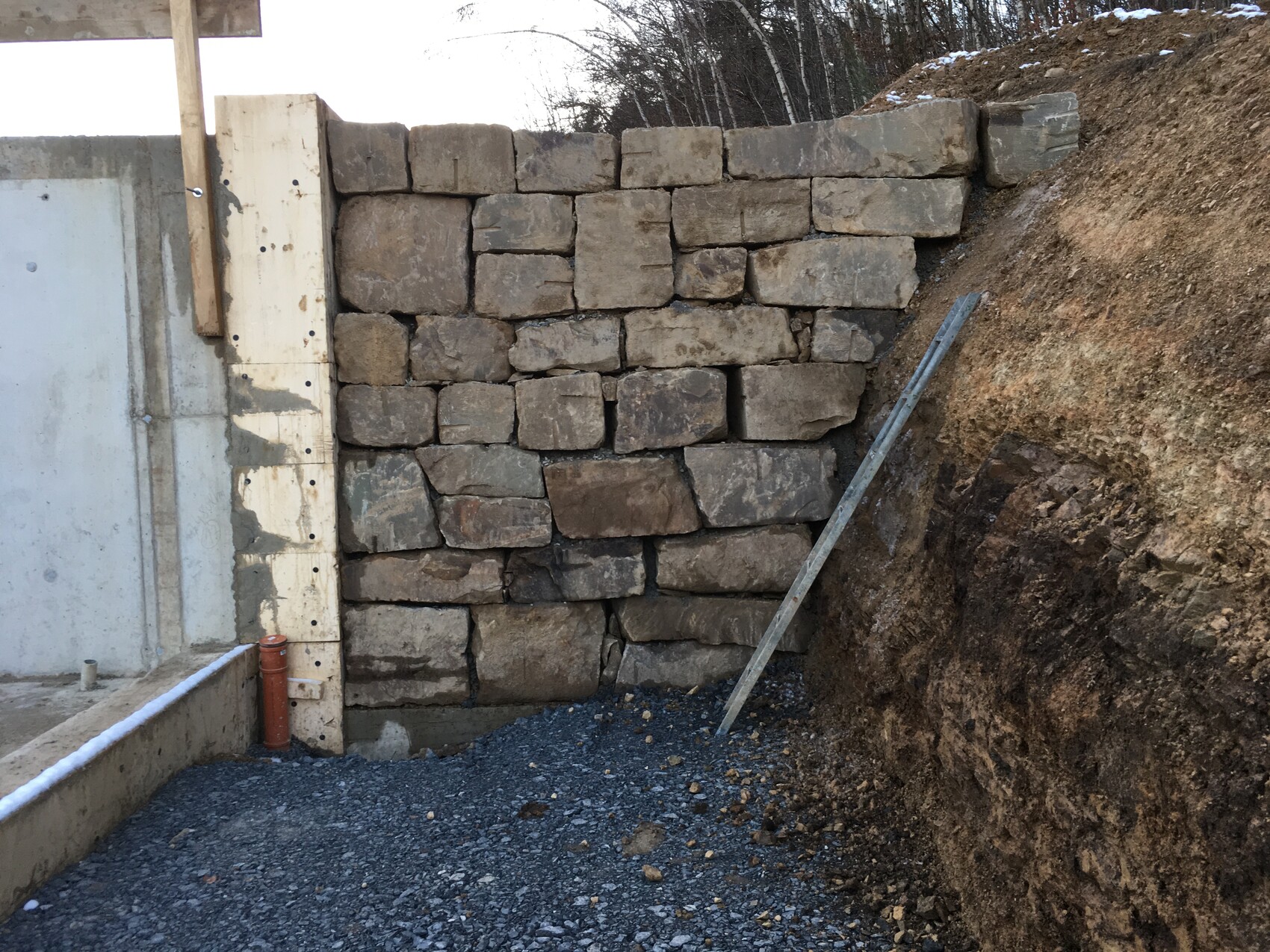 Retaining wall made of large natural stone blocks on an earth embankment, gravel floor at a construction site