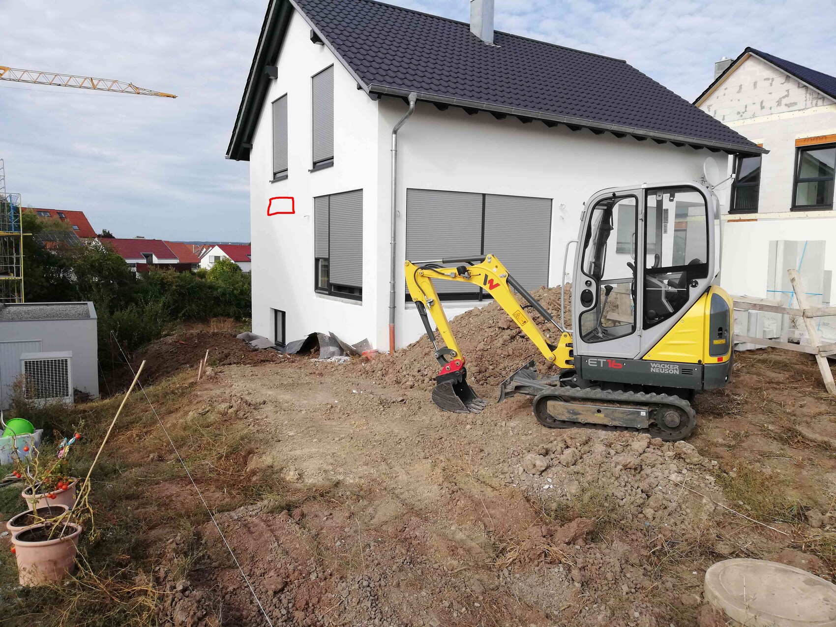 Yellow mini excavator on construction site next to a white house with roller shutters.
