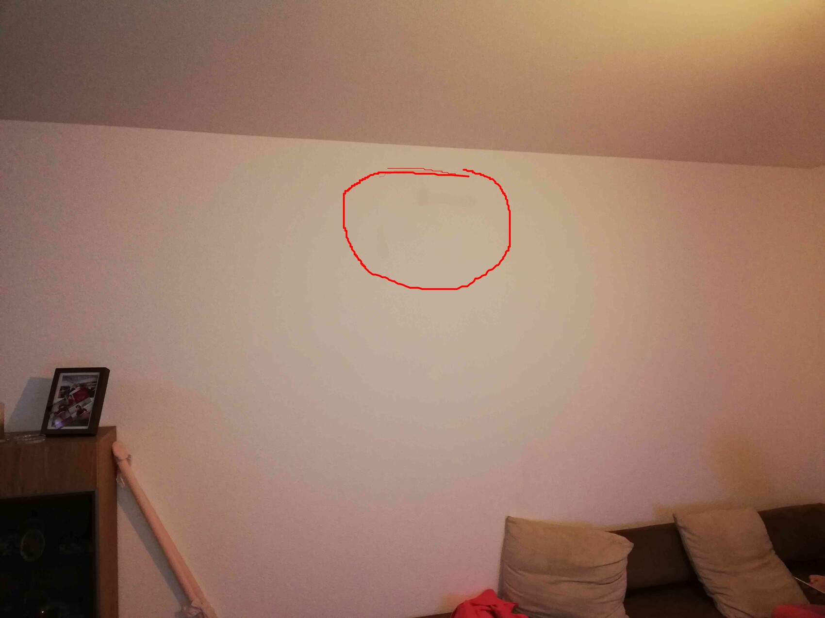 Living room: sofa on the right, cabinet on the left with photo; red circle marks wall stain in the middle.