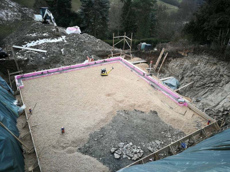 Construction site footing with gravel base, pink polystyrene insulation, excavator on slope