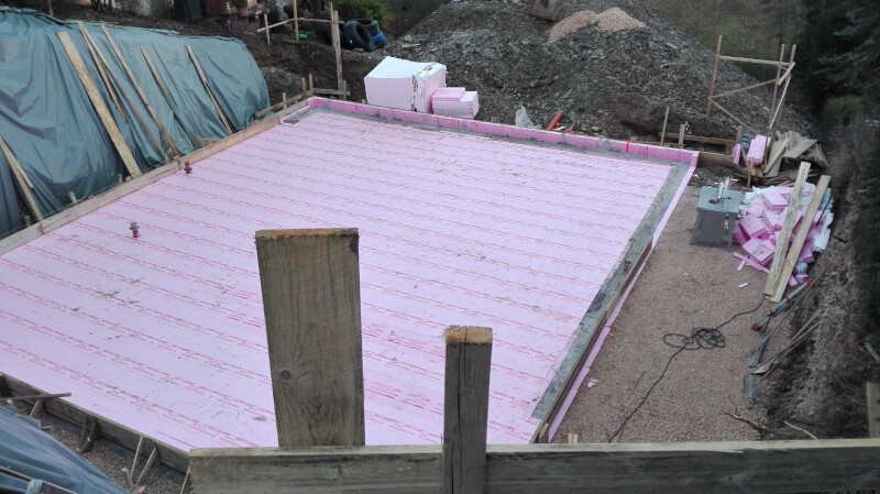 Foundation area with pink polystyrene insulation boards, wooden posts, and construction machinery.