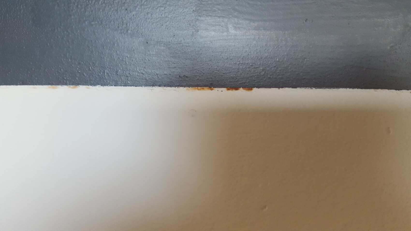 Dark blue upper part meets beige lower part; rust stains along the separation line.
