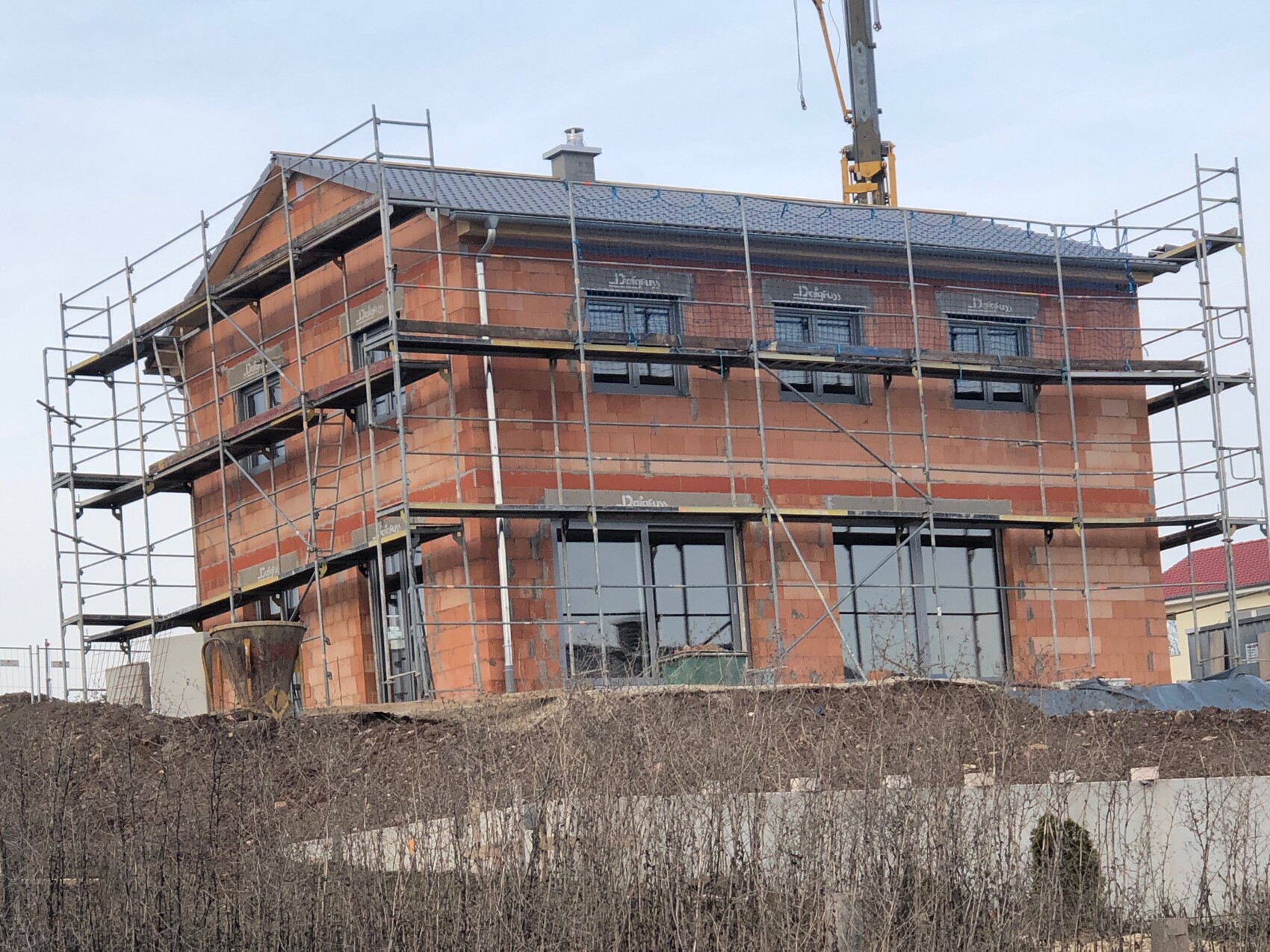 Brick house under construction with scaffolding all around; construction crane in the background