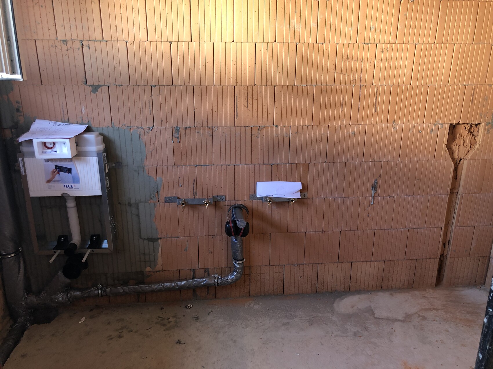 Shell bathroom: brick wall, TECE flush tank, pipes, and flexible stainless steel hose.