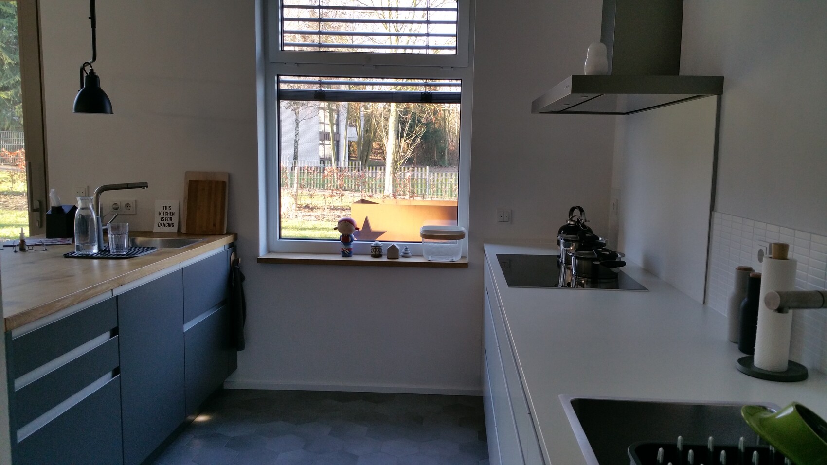 Modern kitchen unit with sink on the left, large window front, stove on the right with extractor hood, garden view.