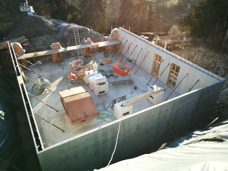 Construction pit with concrete foundation walls, construction equipment, building materials, and tools.