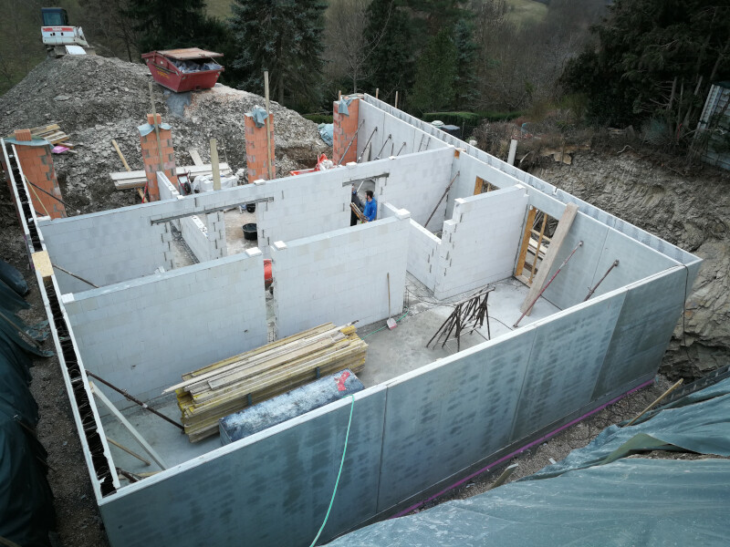 Rohbau eines Hauses: Fundamentswände aus Betonblöcken, Innenräume sichtbar, Arbeiter auf Baustelle