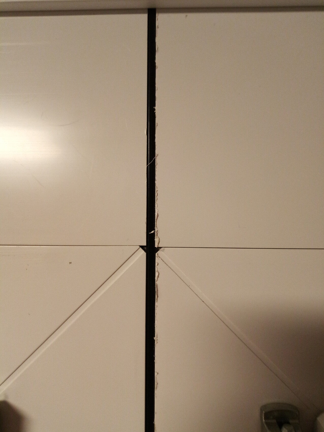 White cabinet doors with a gap at the seam and damaged edge.