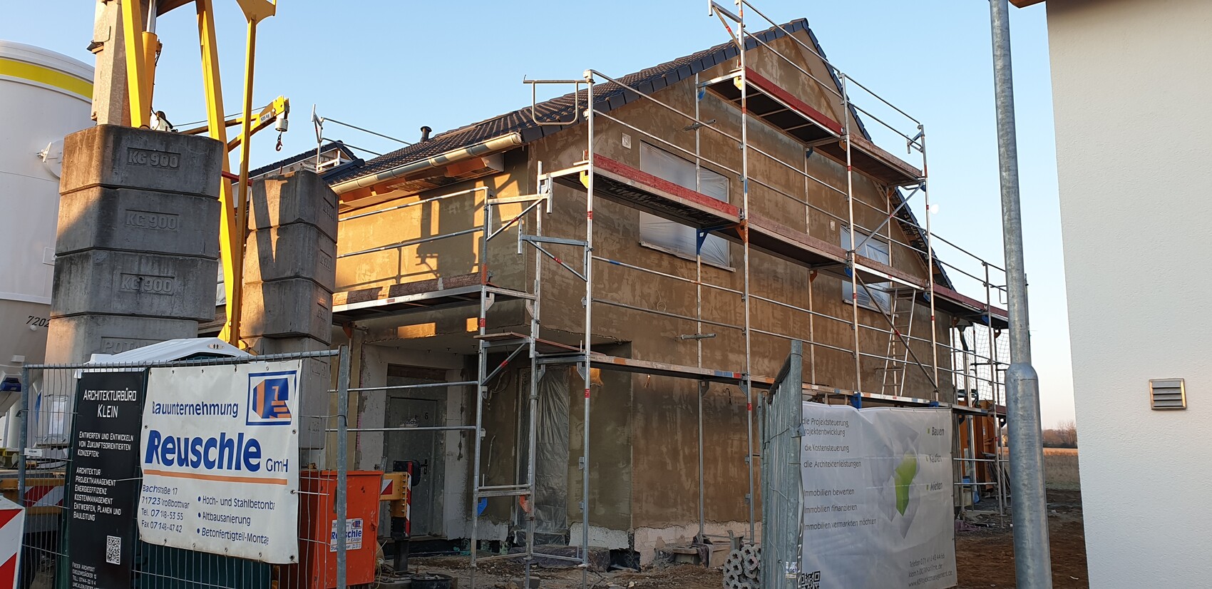 Multi-story house under scaffolding; construction fence banner Reusche GmbH on site.