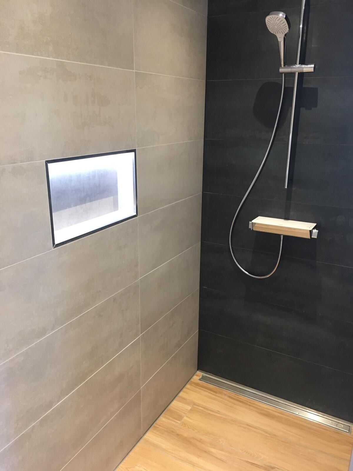 Modern shower: light gray and black tiles, niche, hand shower, wooden shelf