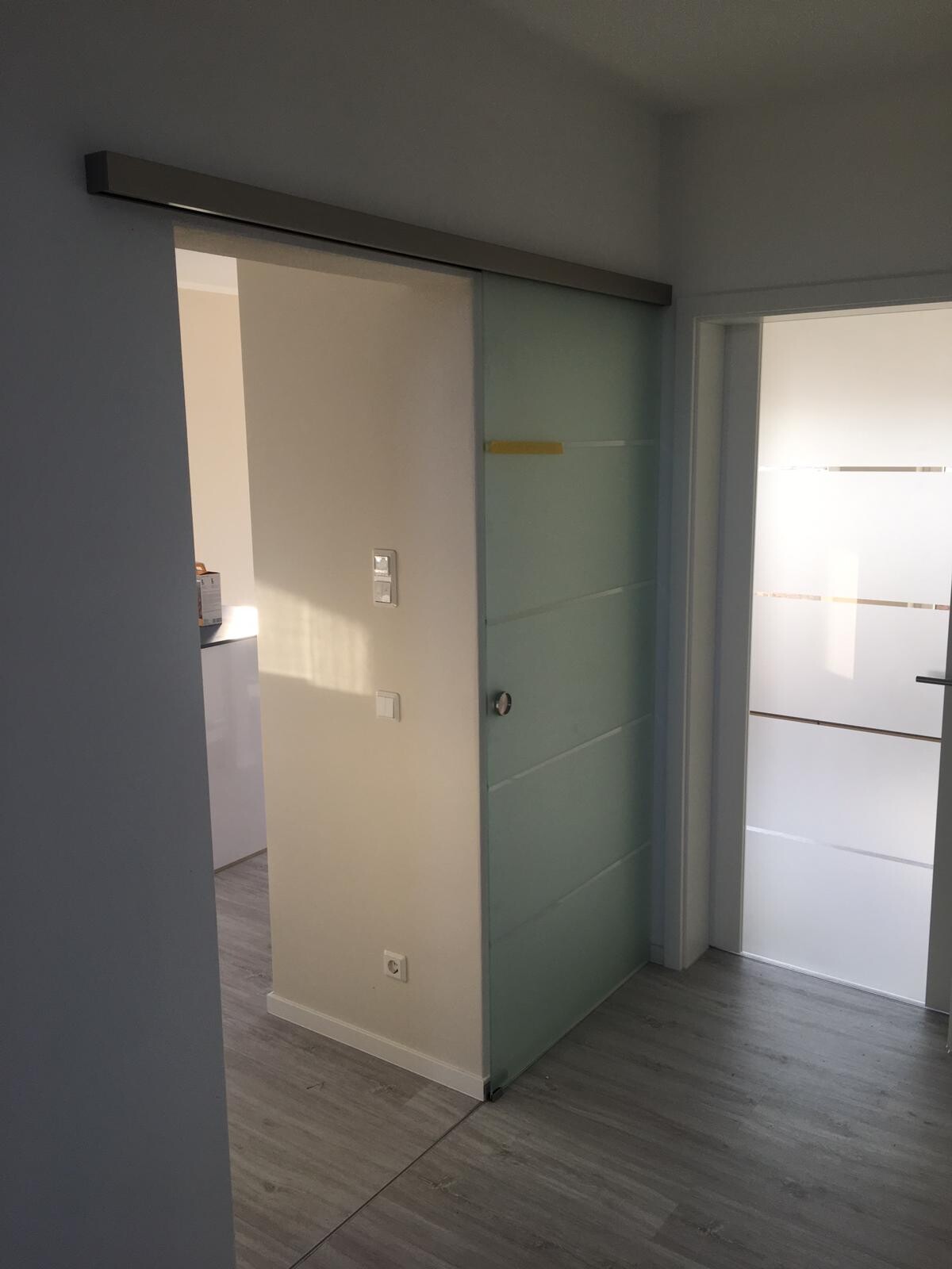 Modern hallway with glass sliding door, bright interior, and gray laminate flooring.