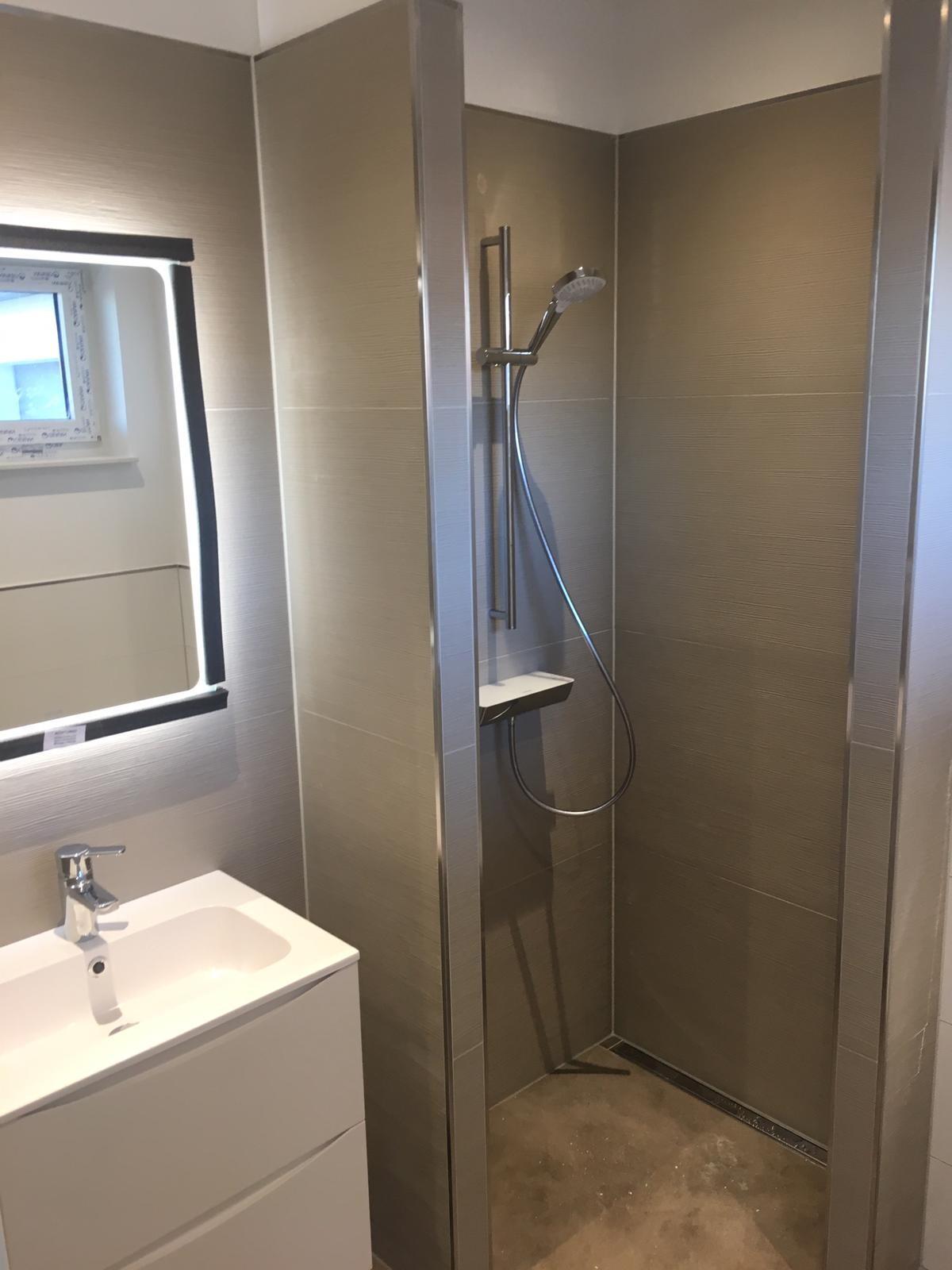 Modern bathroom with shower (metal frame), hand shower, wall tiles, sink, and mirror.