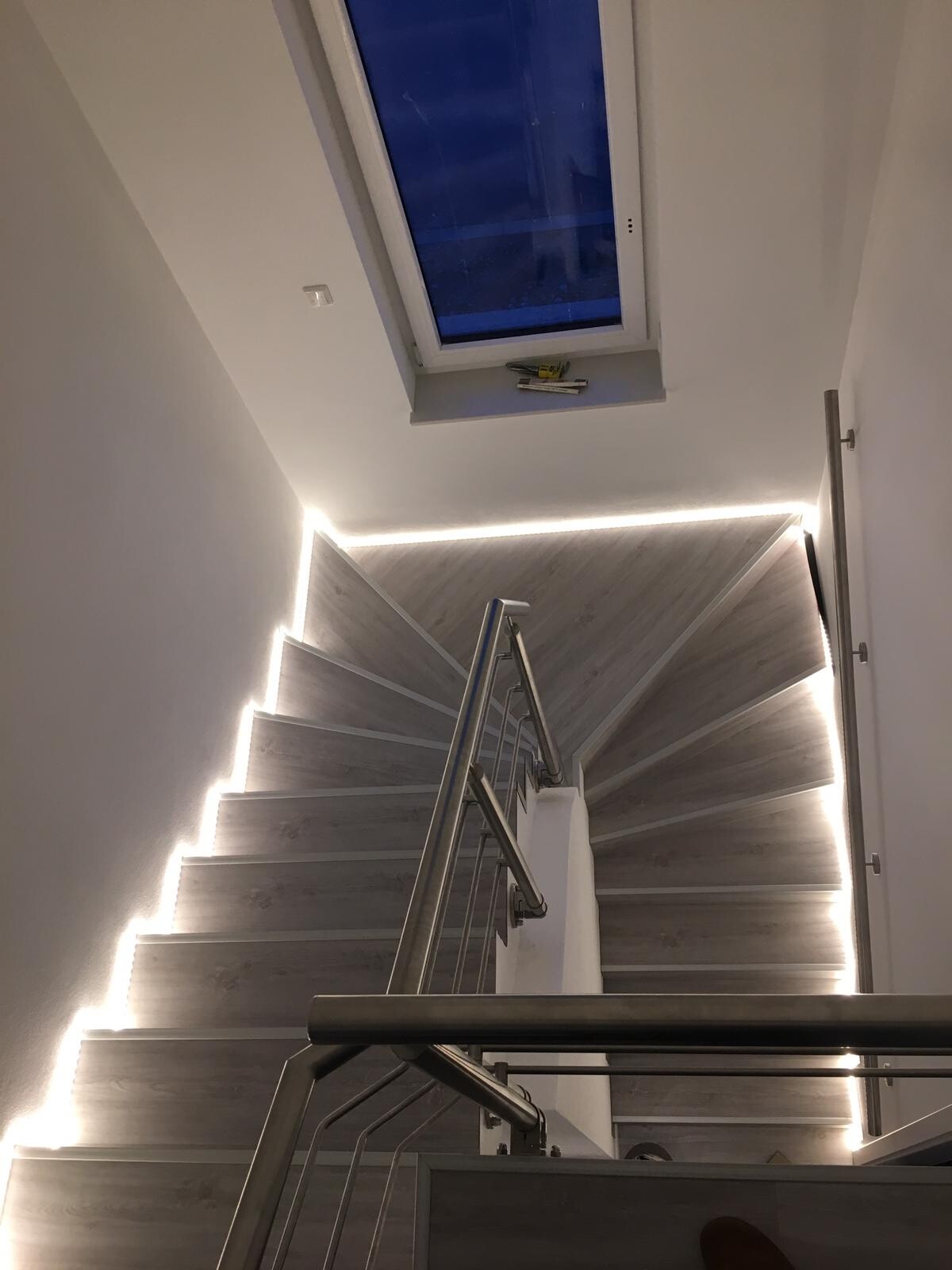 Modern staircase with LED step lighting, stainless steel handrail, and skylight.