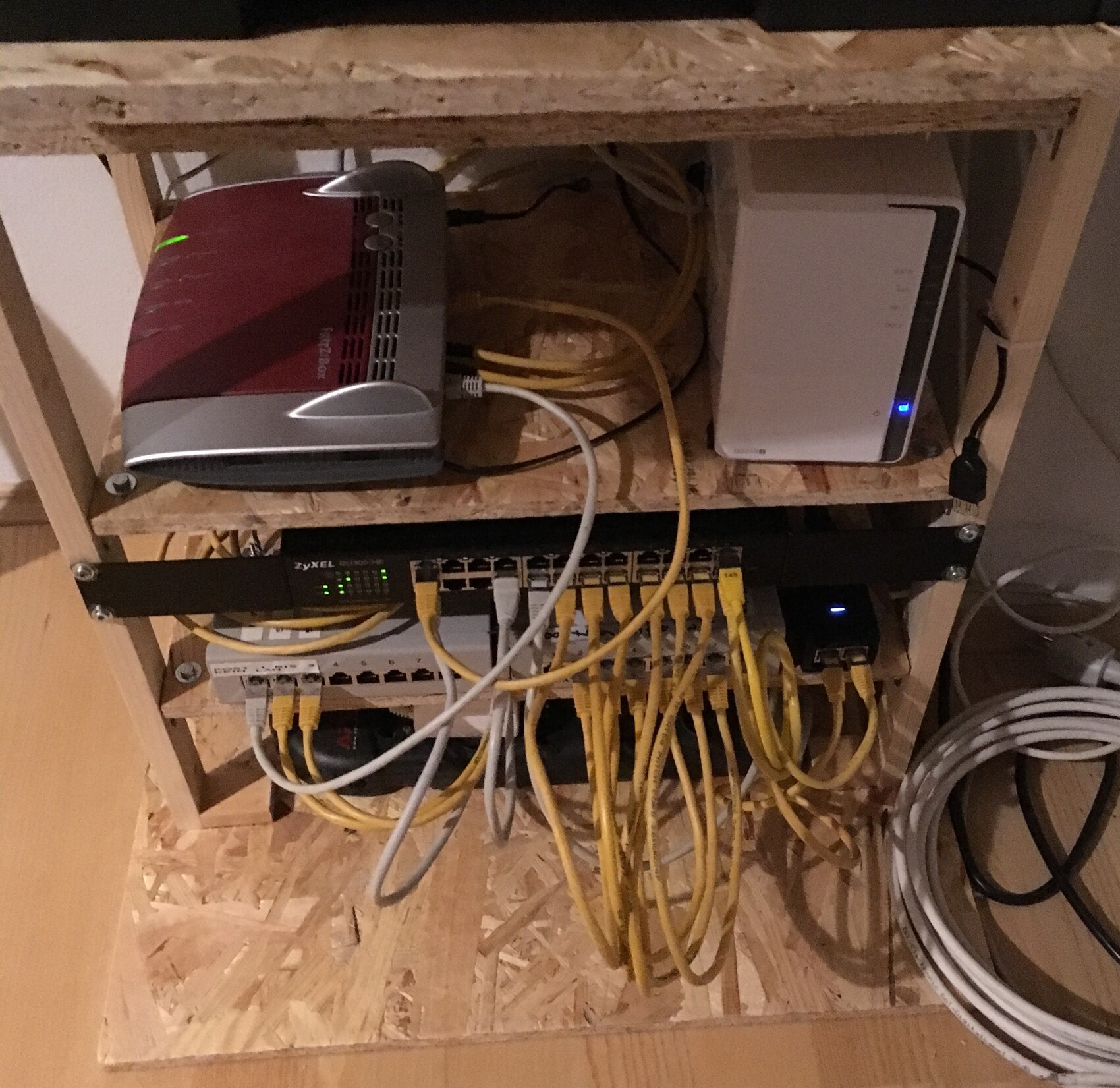 Network router and switch in an open wooden cabinet with many yellow Ethernet cables