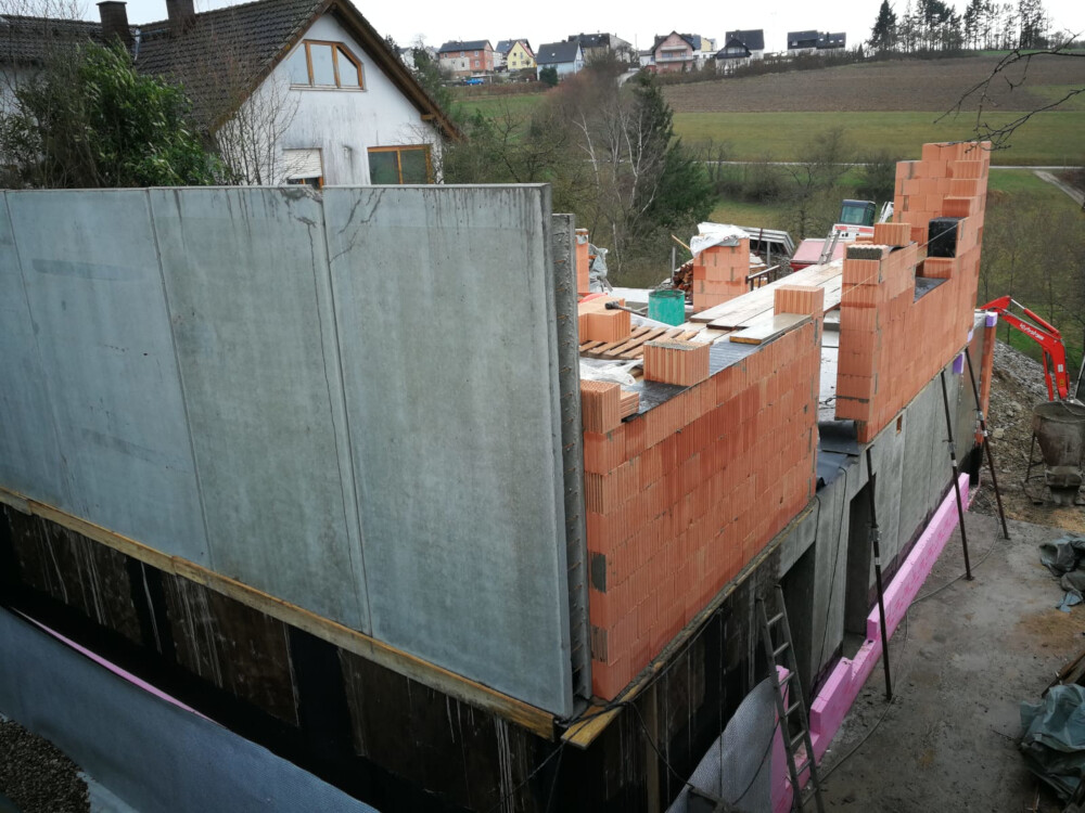Construction site: red brick walls rising on a concrete foundation, materials visible at the building site.