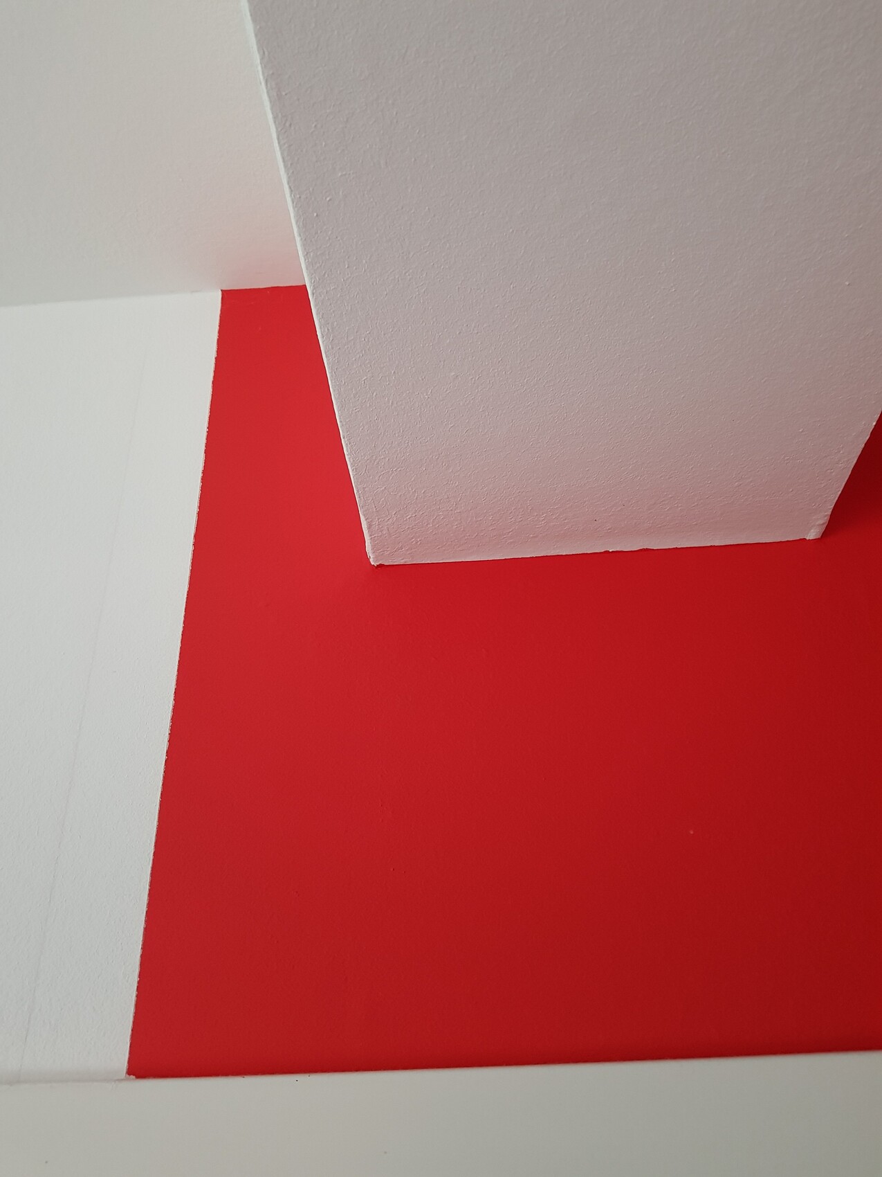 Corner view: red wall meets white, textured ceiling with geometric lines.