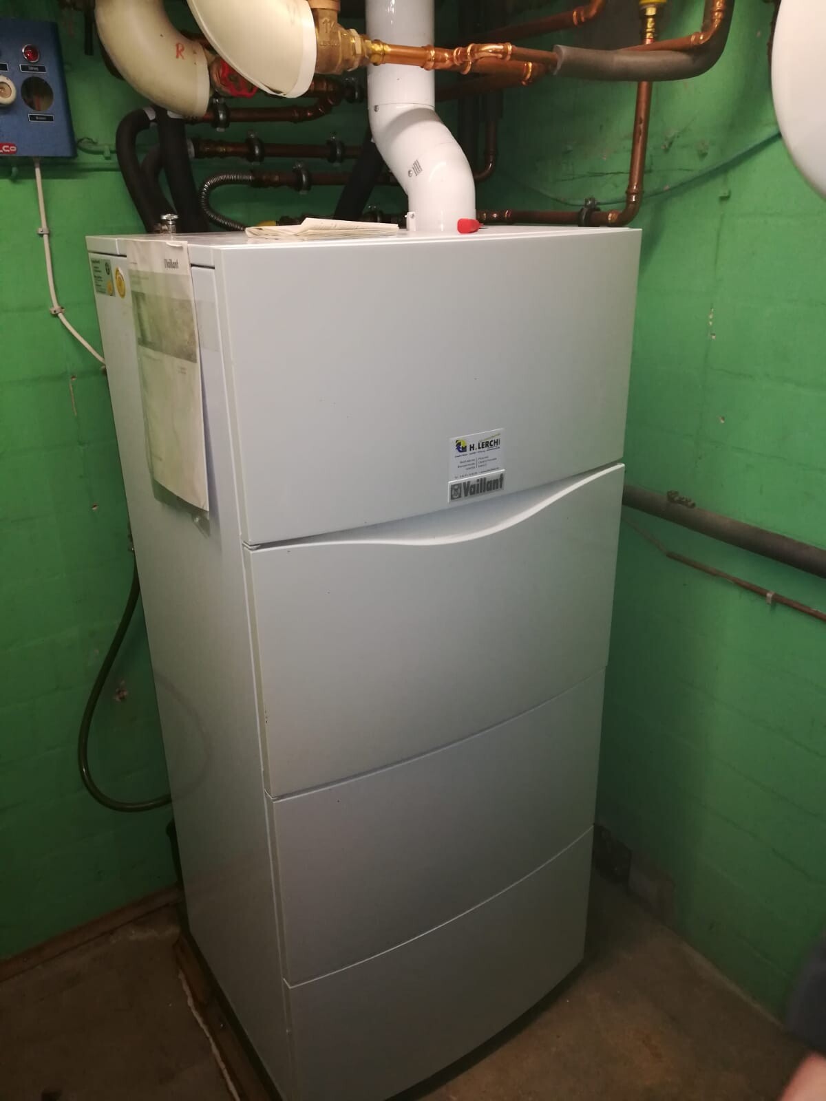Large heating boiler in basement with pipes and green painted walls
