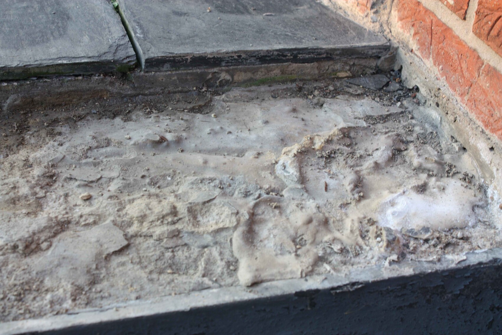 Construction site ground with gravel and concrete debris next to step by red brick wall