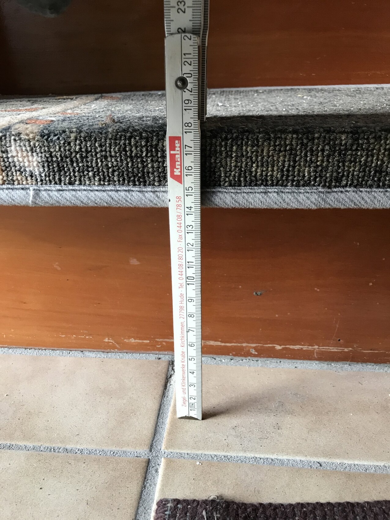 Measuring tape measuring floor covering height between carpet and tiles at door area.