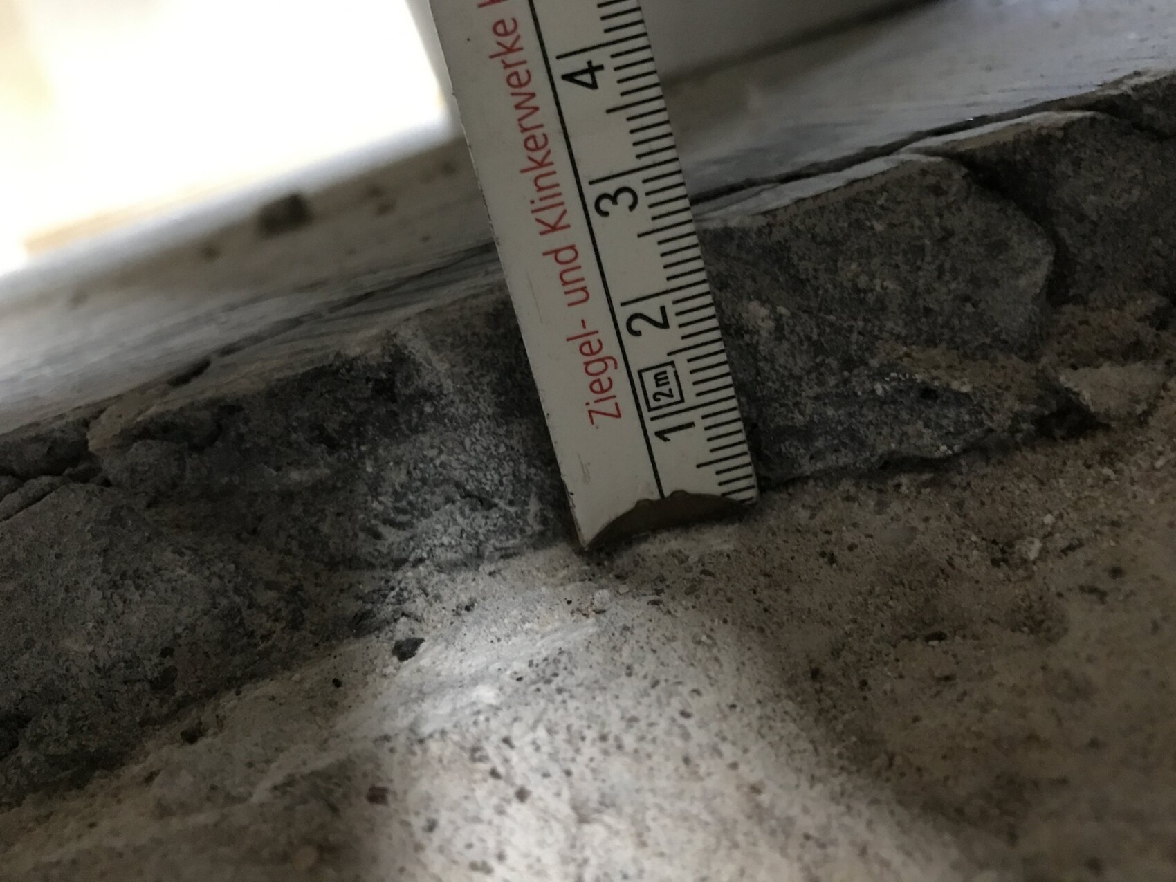 Close-up of measuring tape beside rough masonry and foundation.