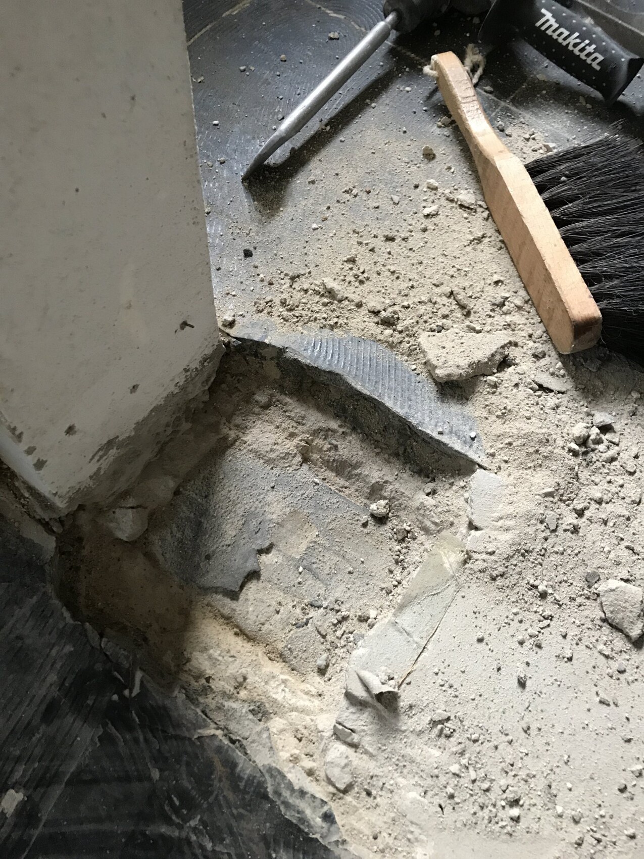 Construction site with dusty concrete floor, broom, and construction tools next to wall.