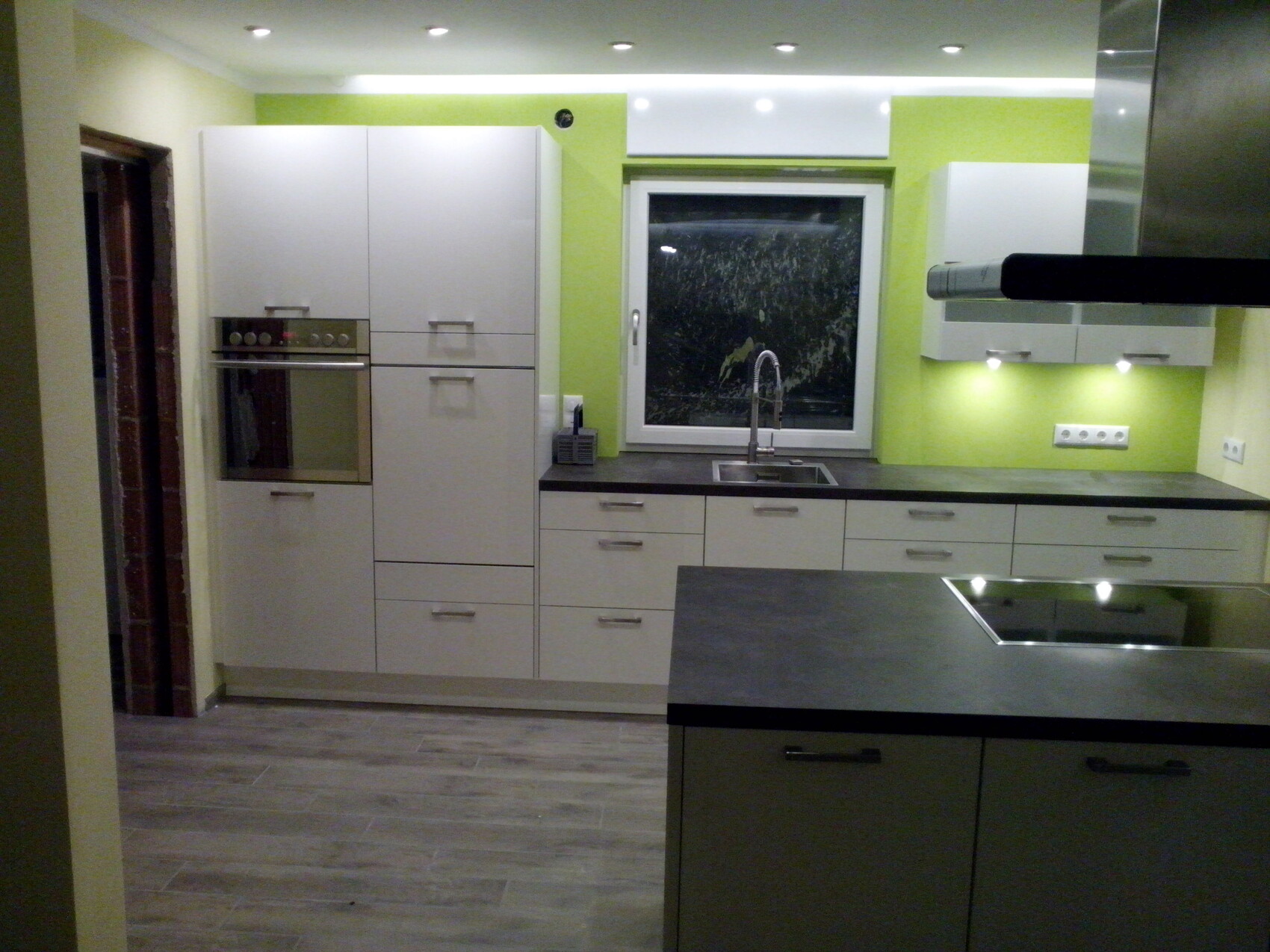 Modern kitchen with white cabinets, oven, sink in front of window, and gray countertops.