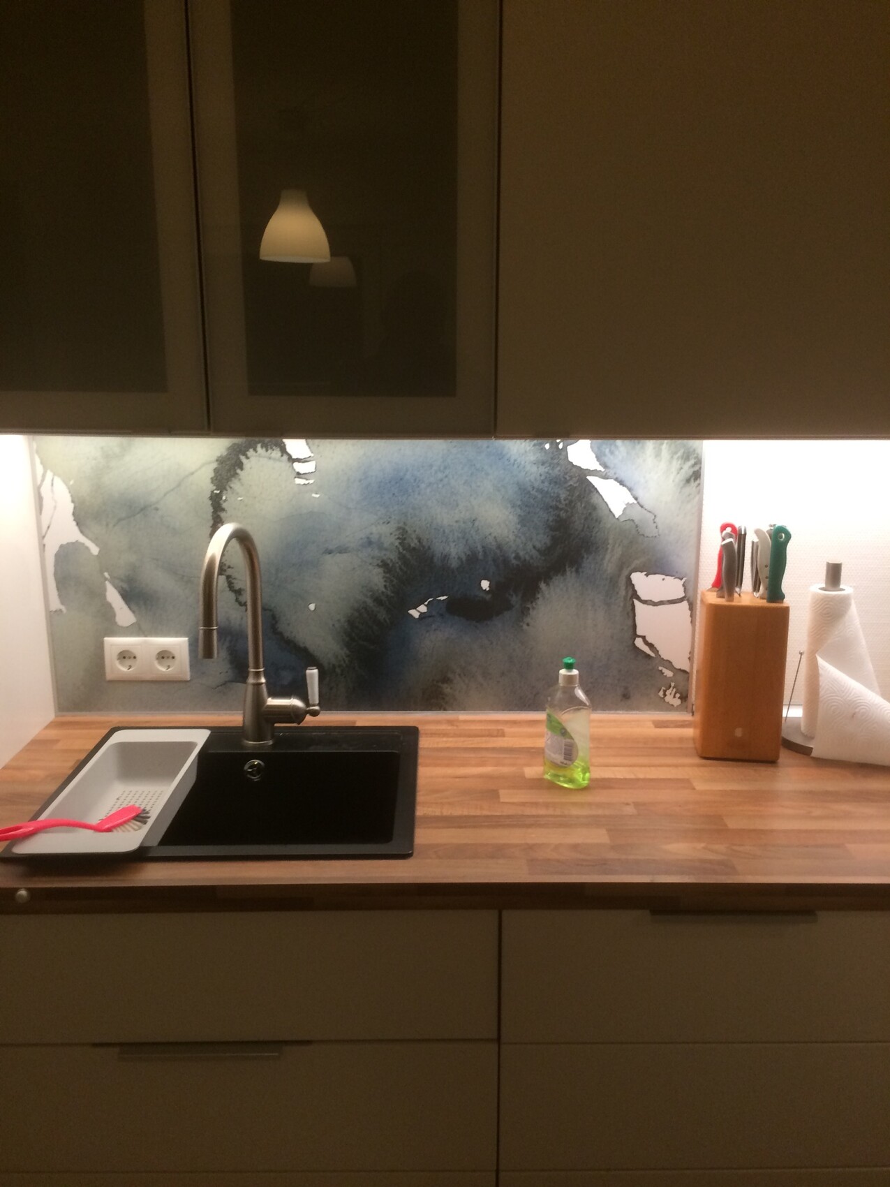 Kitchen countertop with sink, stainless steel faucet, dish soap, knife block, and drying rack.
