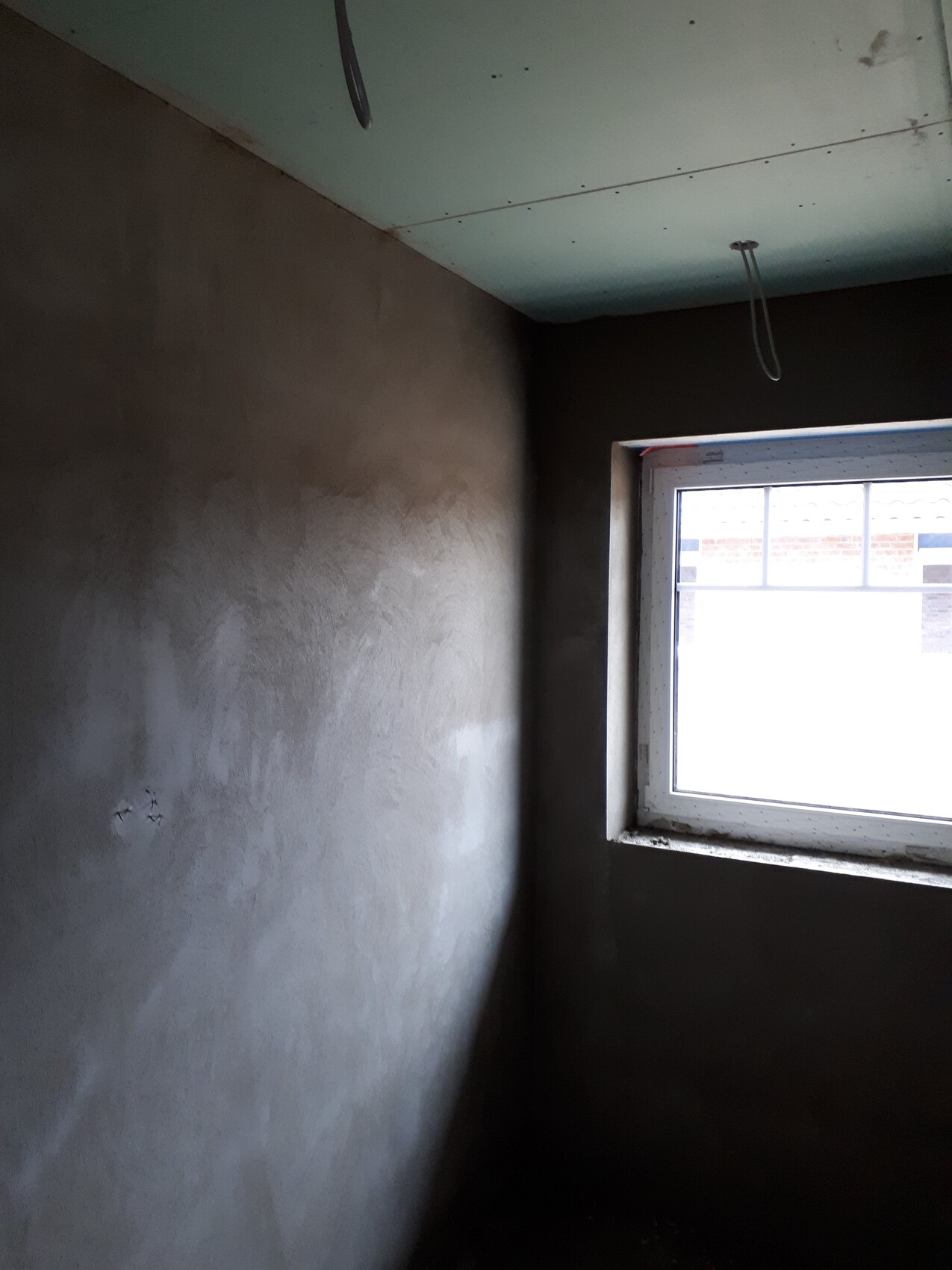 Unfinished room with rough gray walls, greenish ceiling, window on the right; loose cables hanging.