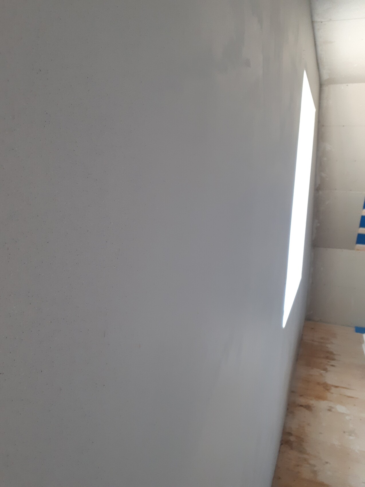 Gray wall with bright vertical light opening on the right, wooden floor, and blue painter’s tape.