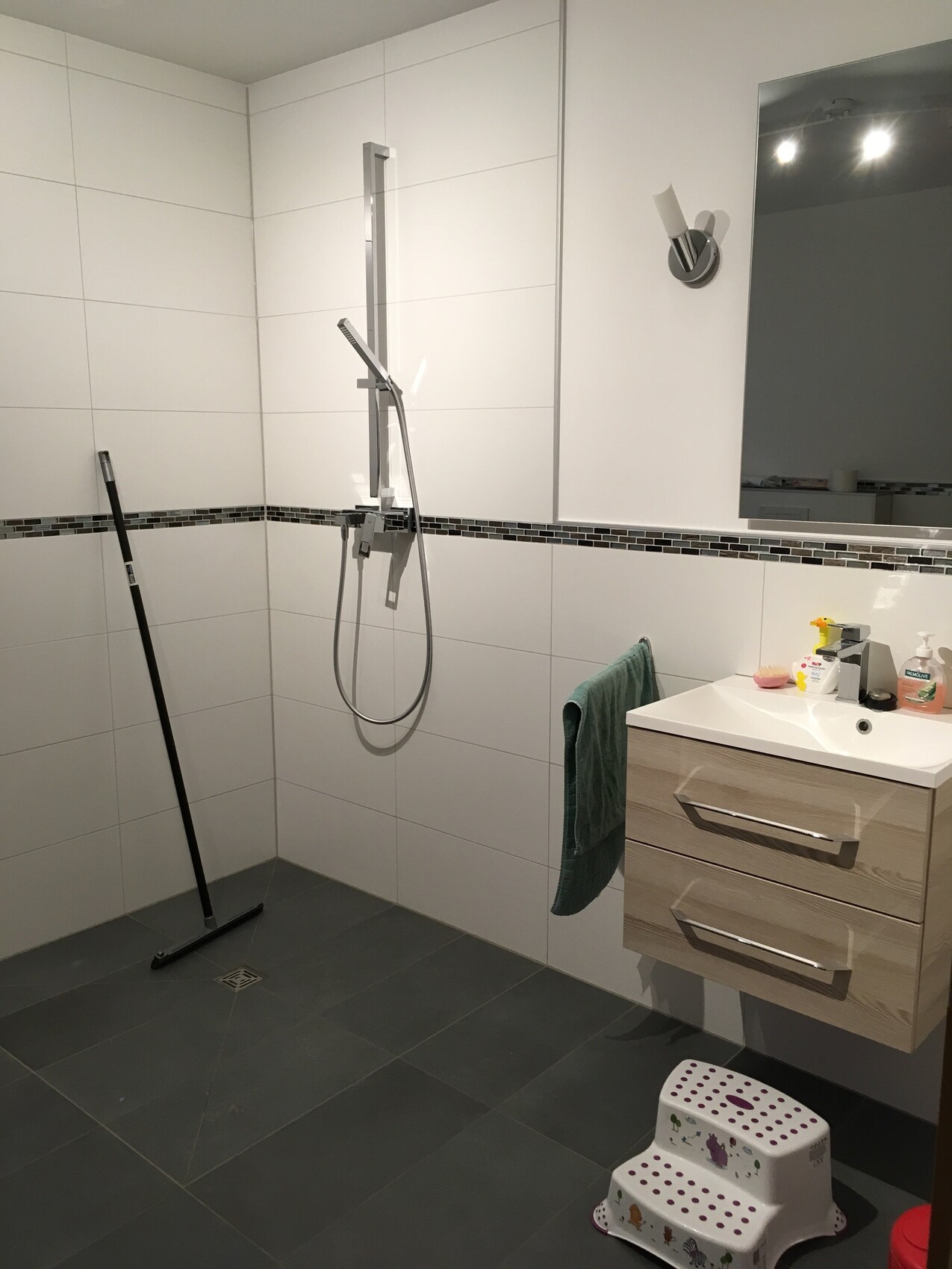 Modern bathroom with shower, washbasin, mirror, towel, and small step stool.