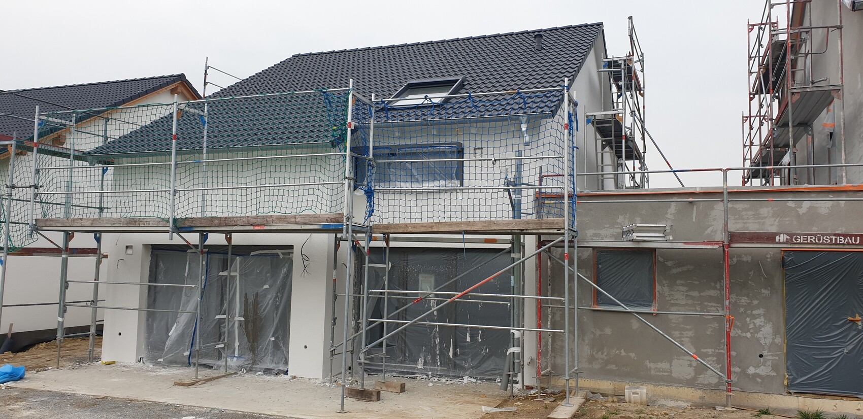 Baustelle mit Gerüst um ein Gebäude; Bauarbeiten, Fenster mit Folie abgedeckt.