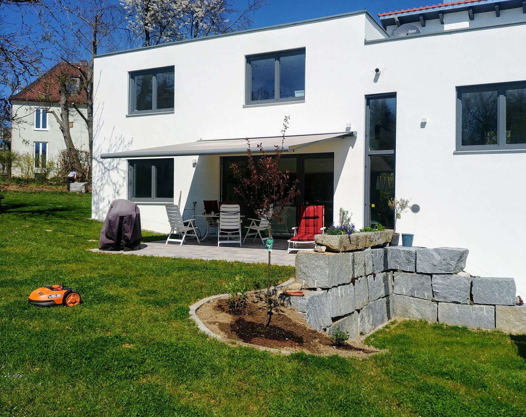 White modern villa with terrace, seating area, covered grill, stone wall, and lawn.