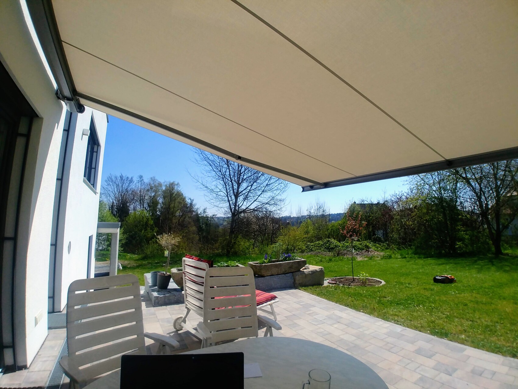 Terrace with retractable awning, garden view, white façade, chairs, and table with laptop