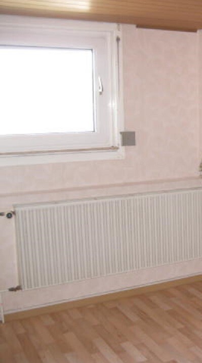 Living room with window, radiator below, wooden floor and light-colored walls