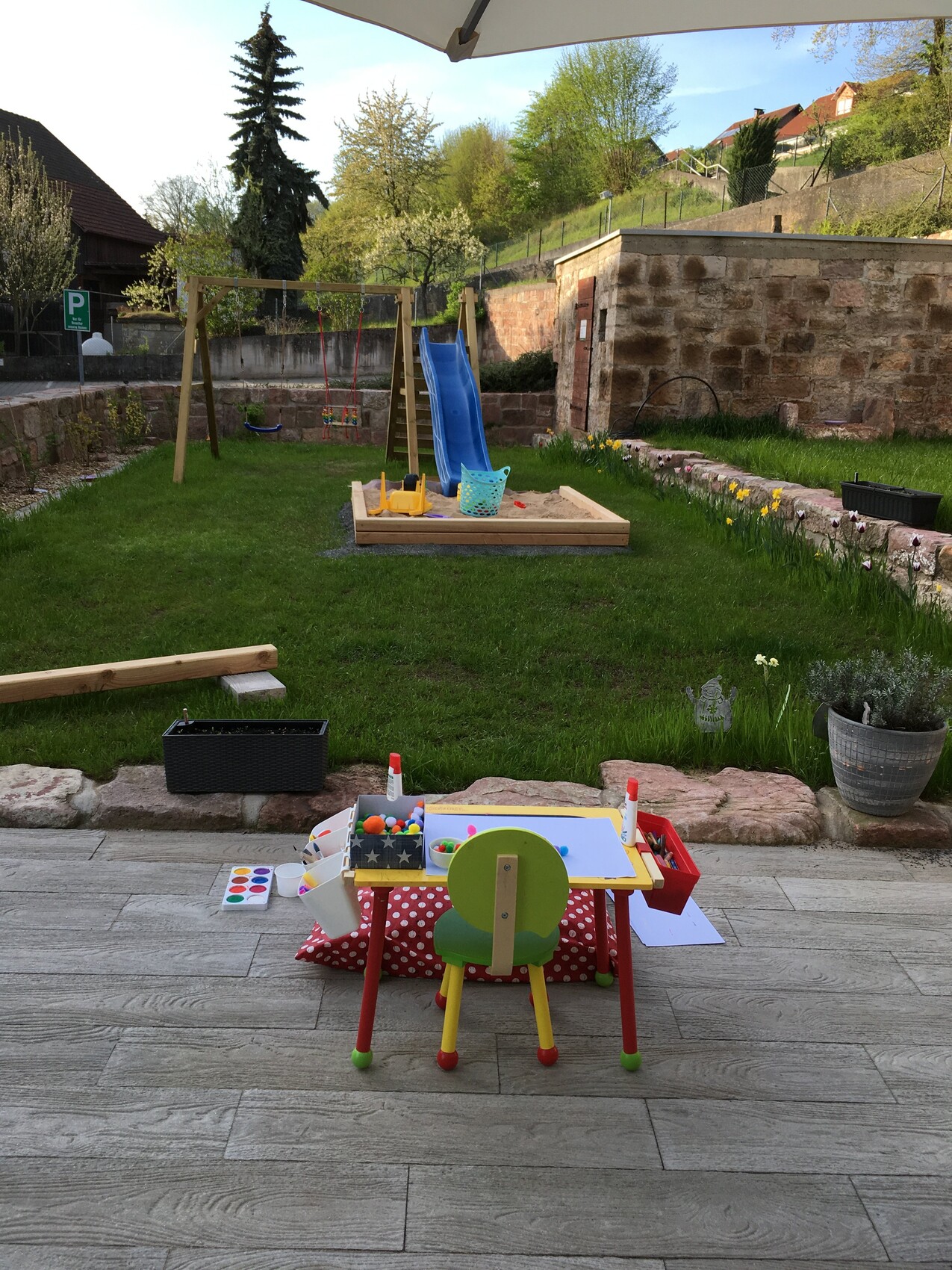 Garden with play area: sandbox, blue slide, swing, and painting area.