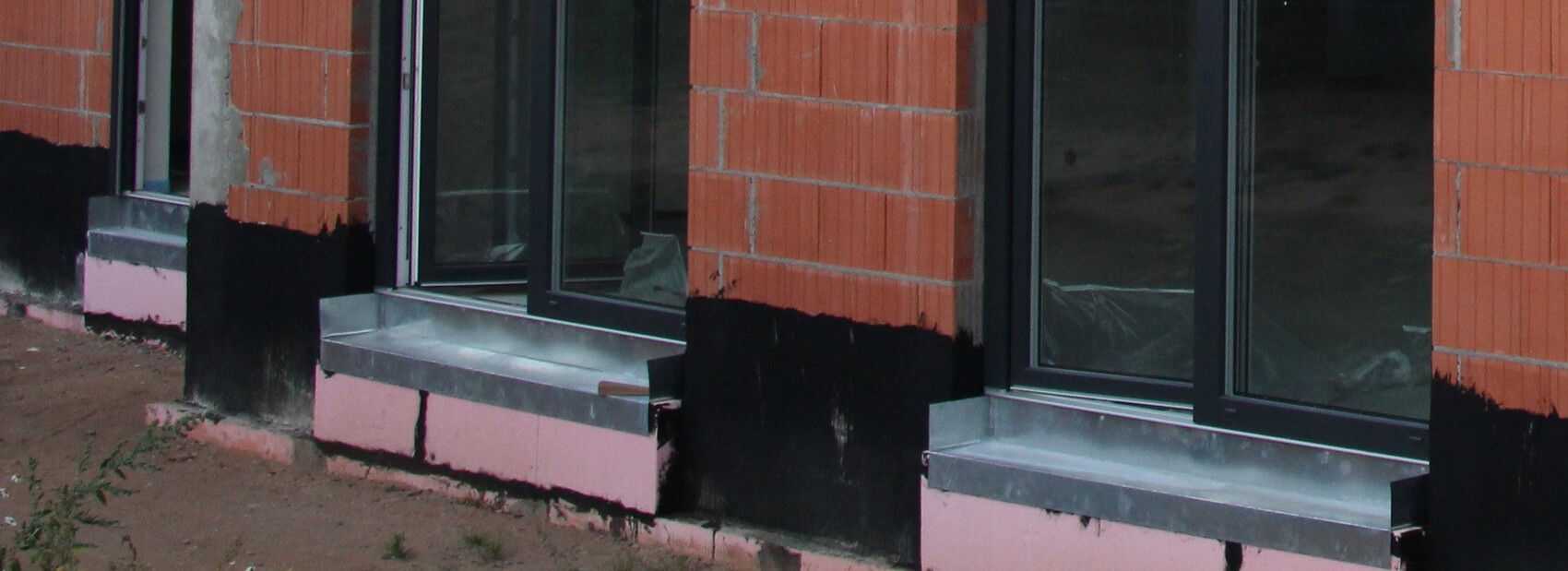 Exterior view of a shell construction with red bricks, black seals at the base, and glass windows.