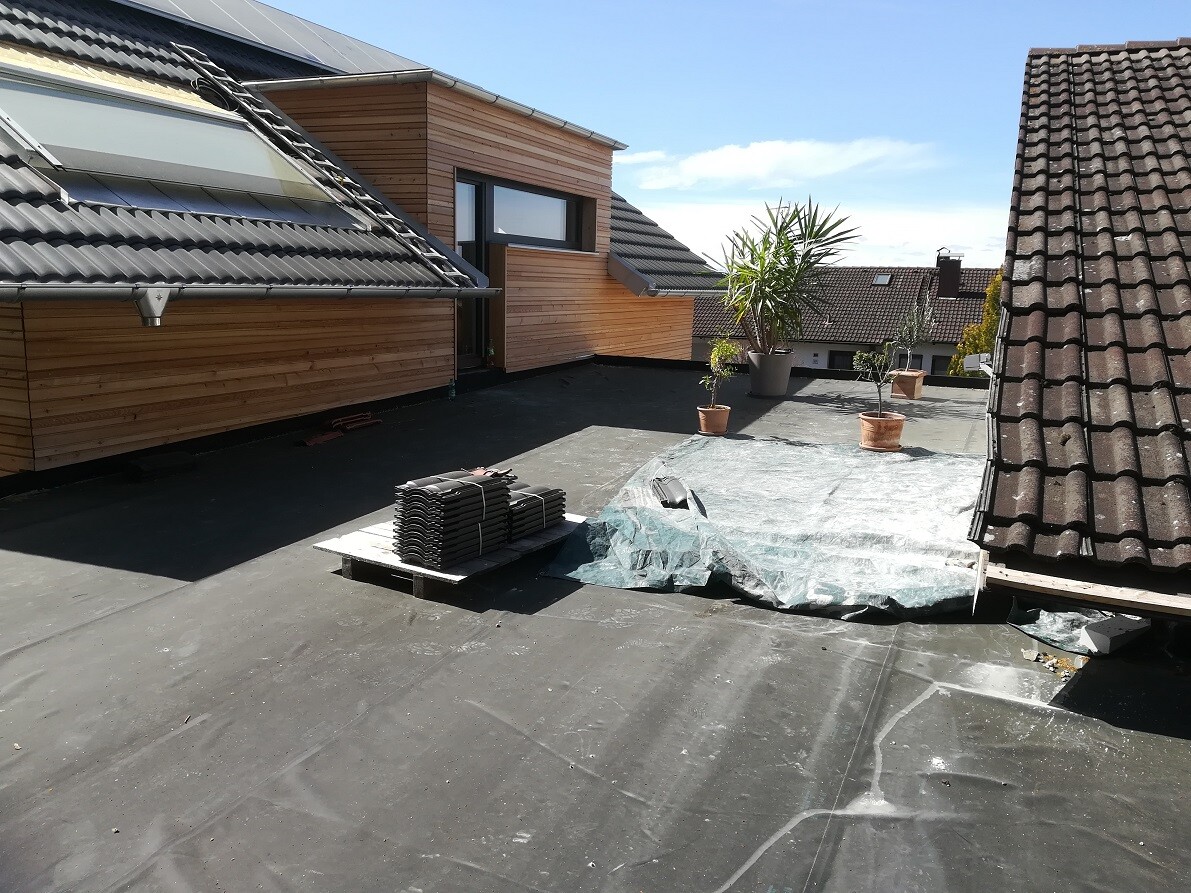 Roof terrace with wooden cladding, potted plants, and pallets with roof tiles.