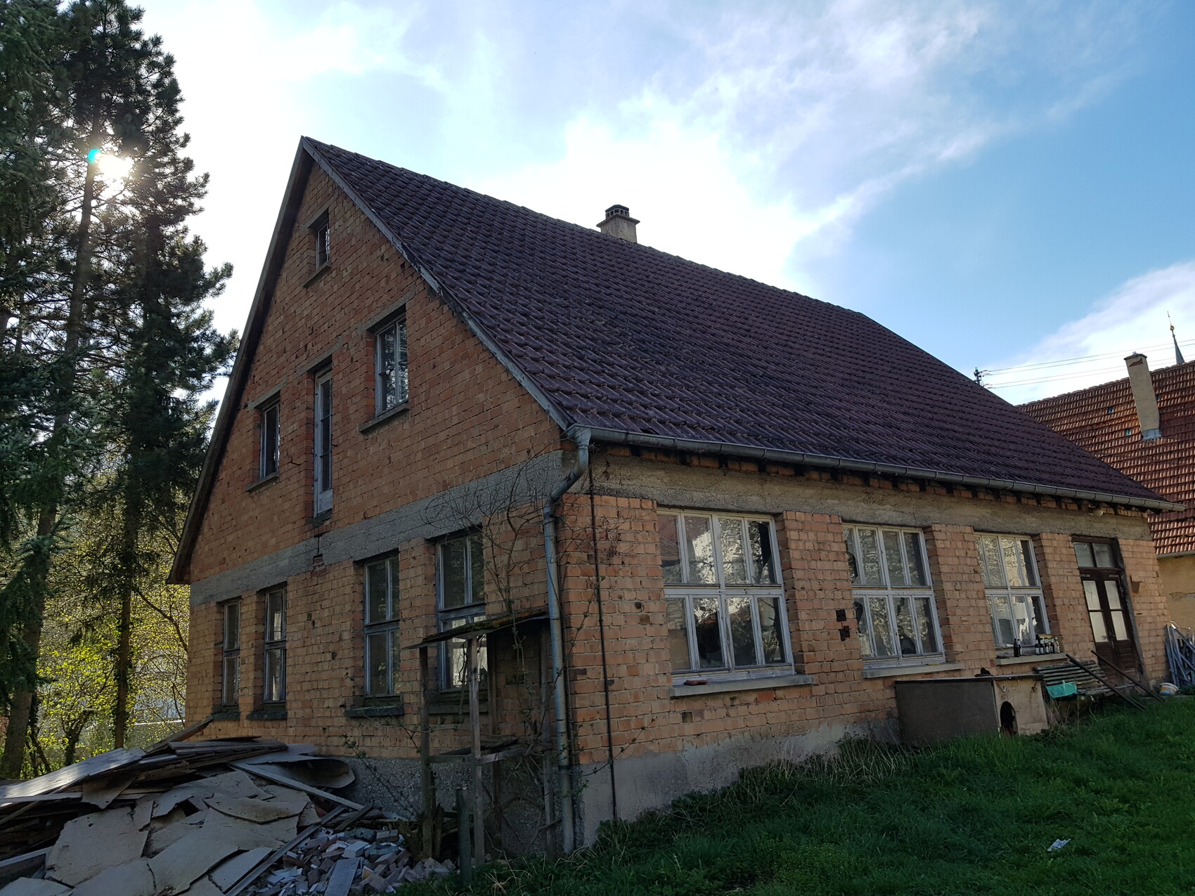 Old brick house with pitched roof, construction debris in the foreground and surrounding trees.
