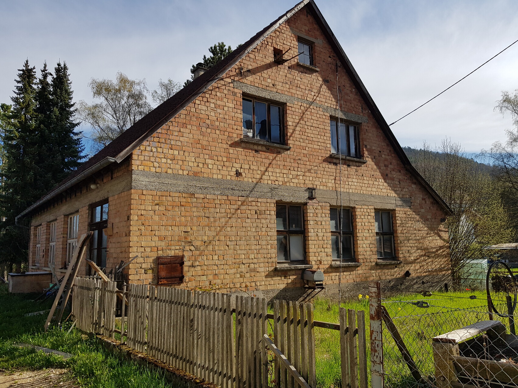Exterior view of a brick house under construction with a roof, windows, wooden fence and garden