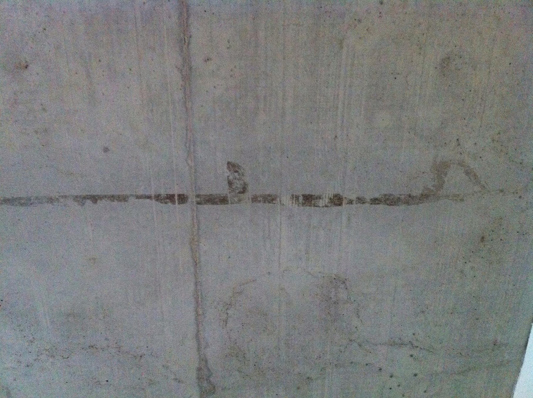 Concrete wall with a horizontal dark line and visible cracks.