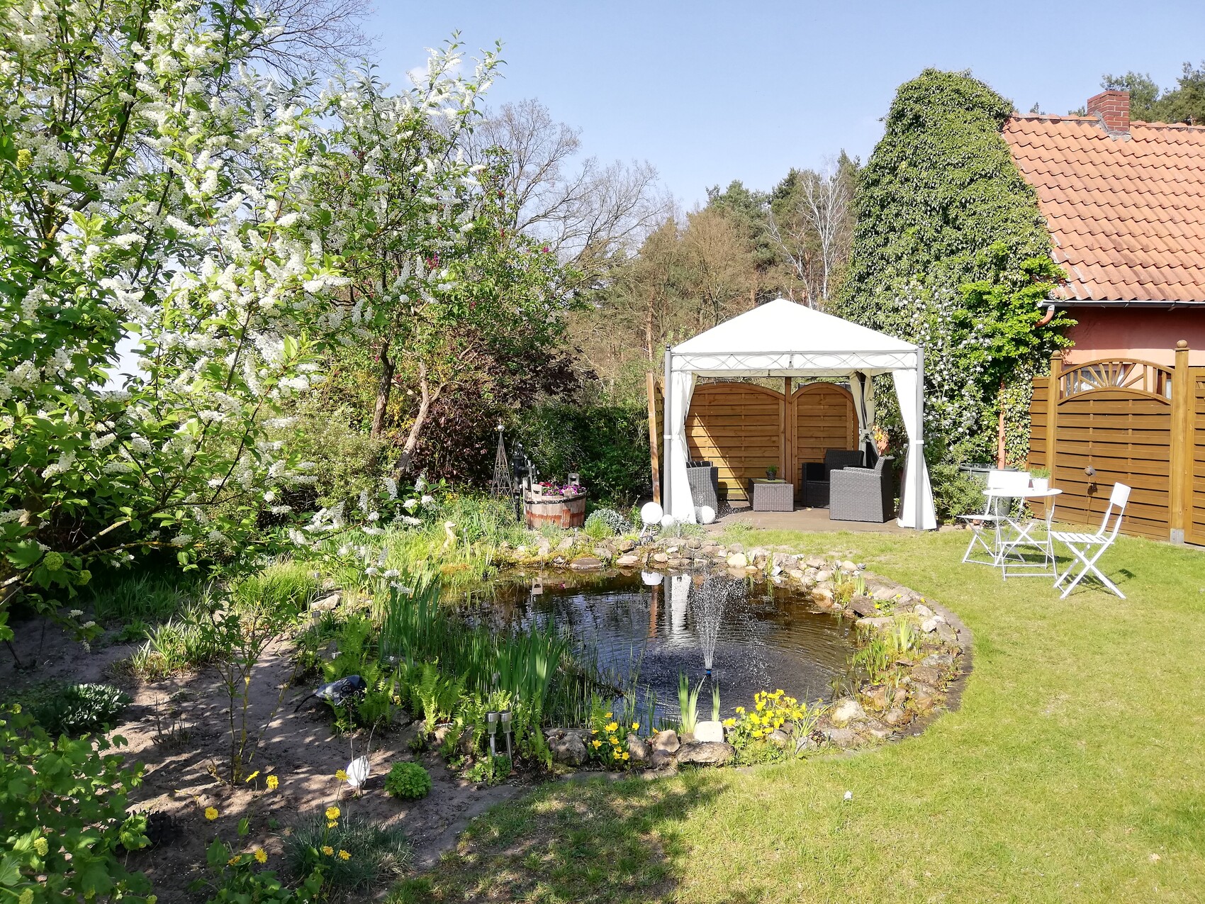 Garten mit Teich, Springbrunnen, weißem Pavillon und Gartenmobiliar im Grünen.