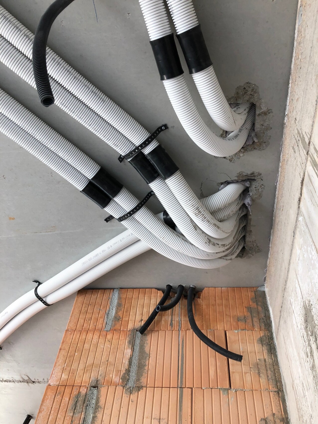 White flexible pipes and black cable conduits in the shell construction, building services installation