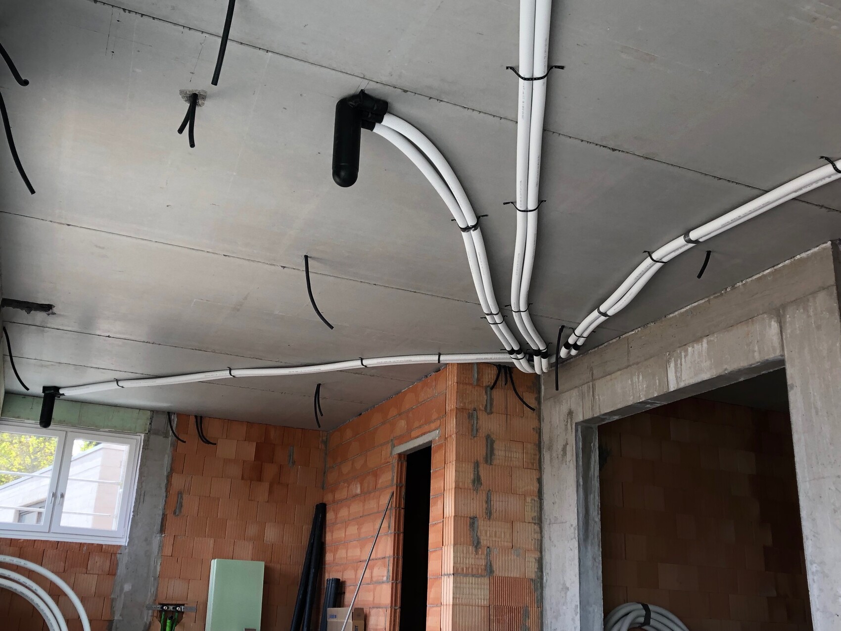 Unfinished room: White cable conduits running along the ceiling, black brackets, brick walls.