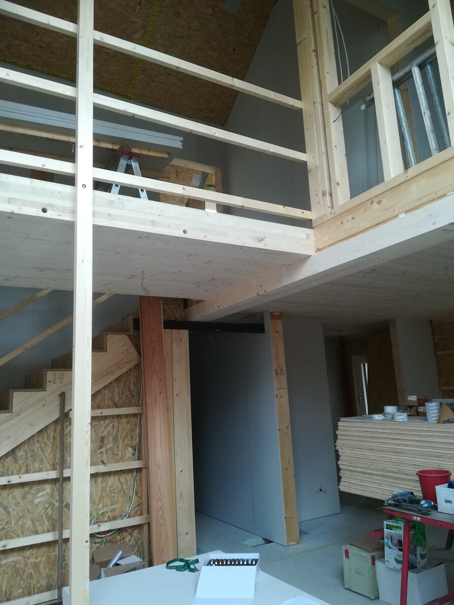 Interior of a new build: wooden structure, staircase, mezzanine railing, construction materials.