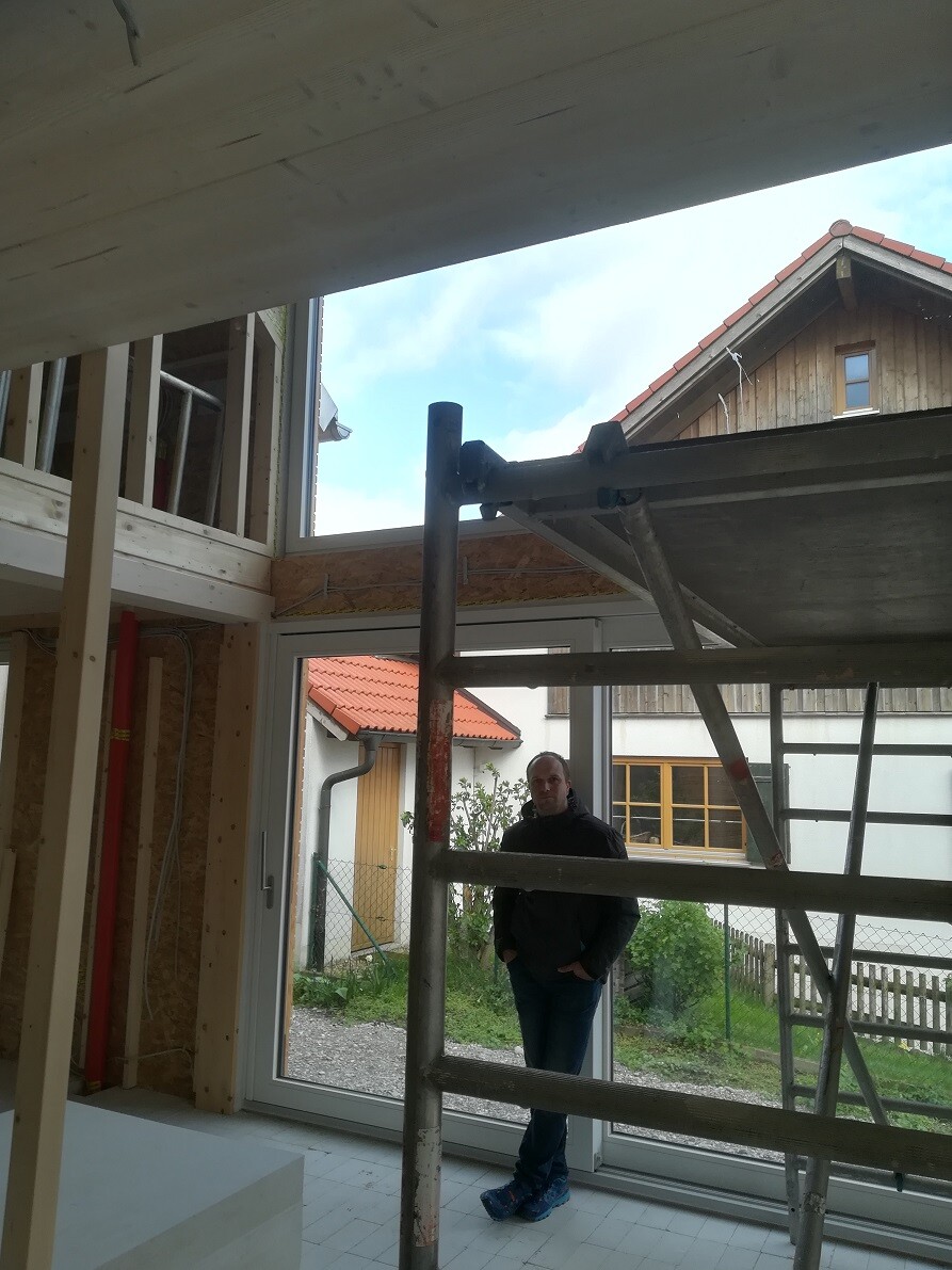 Man standing inside a new build behind scaffolding, large glass facade, view outside.