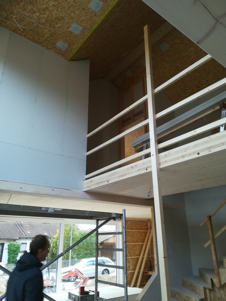 New build shell: interior with wooden gallery, railing, staircase and construction worker in the foreground.
