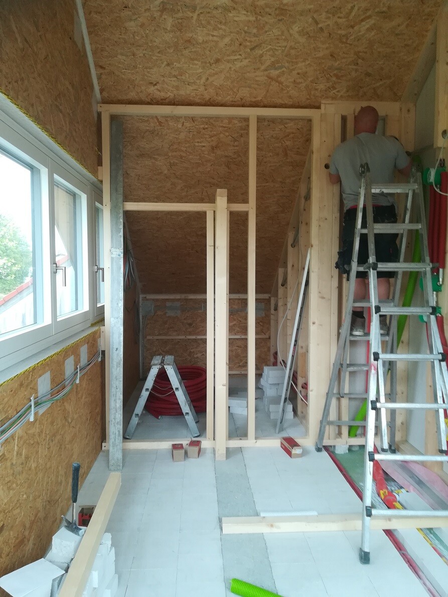 Construction site: Timber stud wall under construction, worker on ladder, tools and materials.
