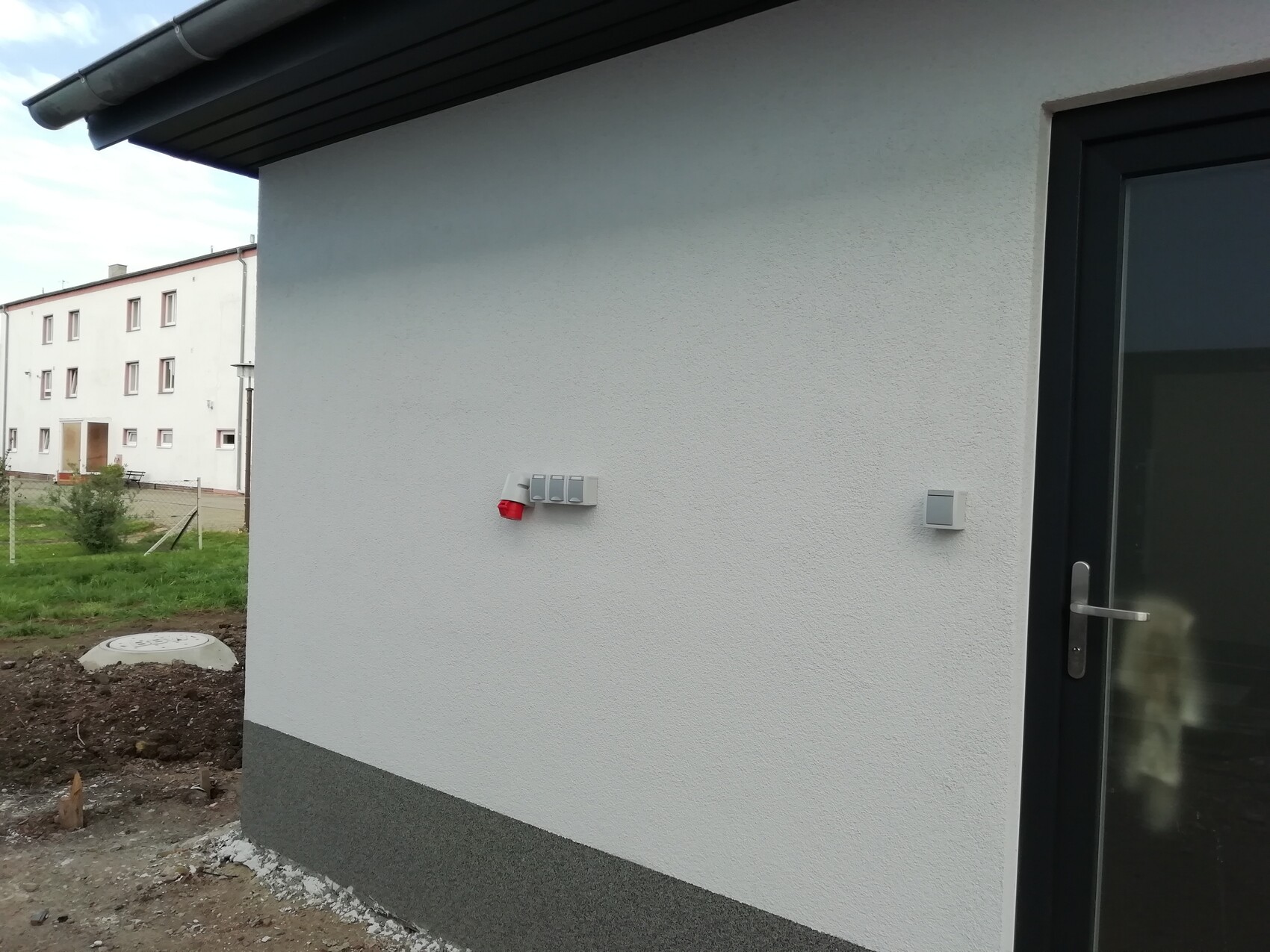 White building facade with door on the right, gray switch boxes and red cover.